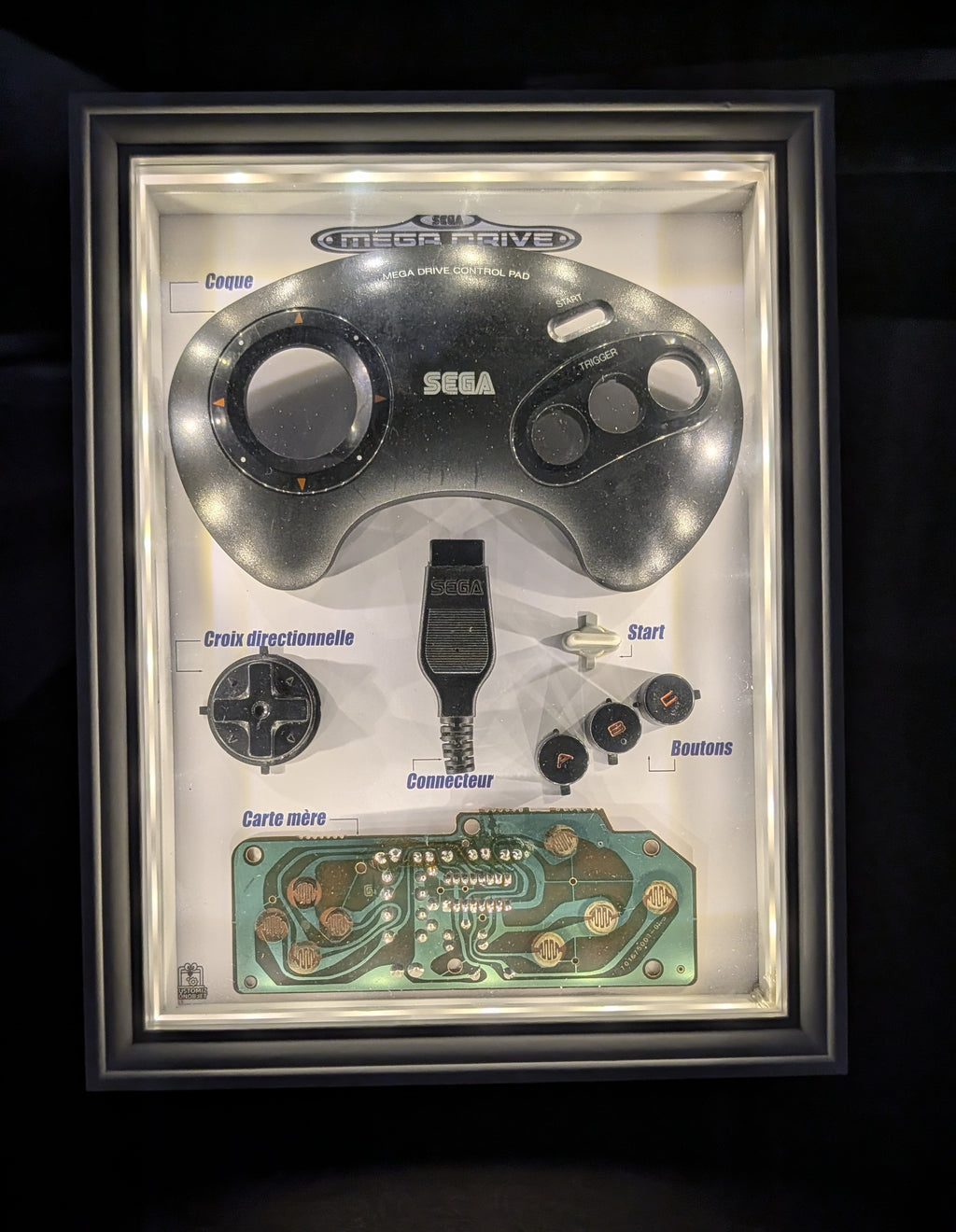 Diorama lumineux SEGA Mega Drive avec véritable manette démontée, composants exposés et éclairage LED intégré